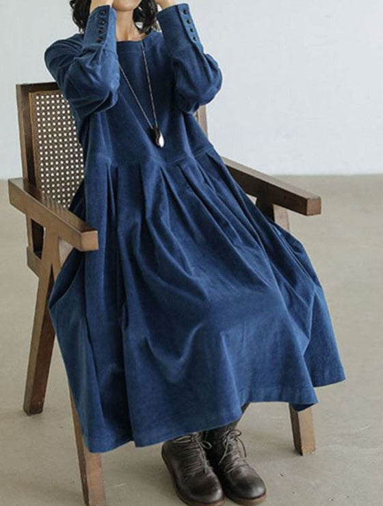 Robe longue bleu jean ample à manches longues, femme assise sur chaise, vue trois-quarts, look casual chic avec bottines