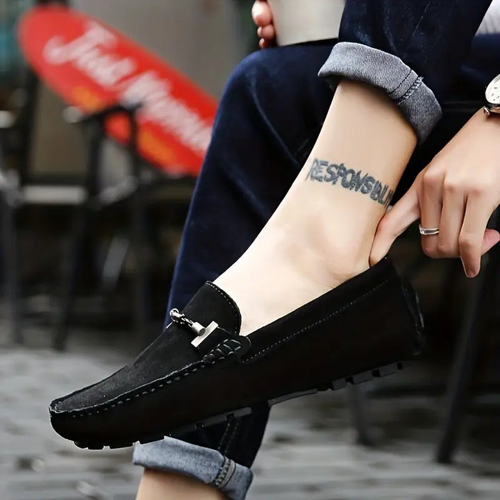Homme portant des mocassins noir sophistiqués avec détail métallique, semelle souple et pantalon retroussé