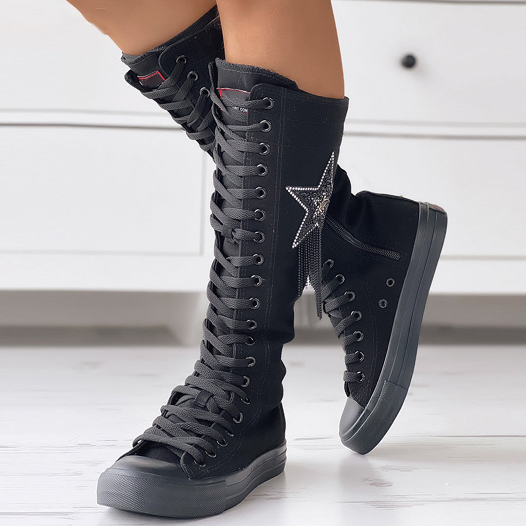 Bottes sneakers noires montantes pour femme, portées de profil avec fermeture à lacets, étoile latérale et semelle épaisse.