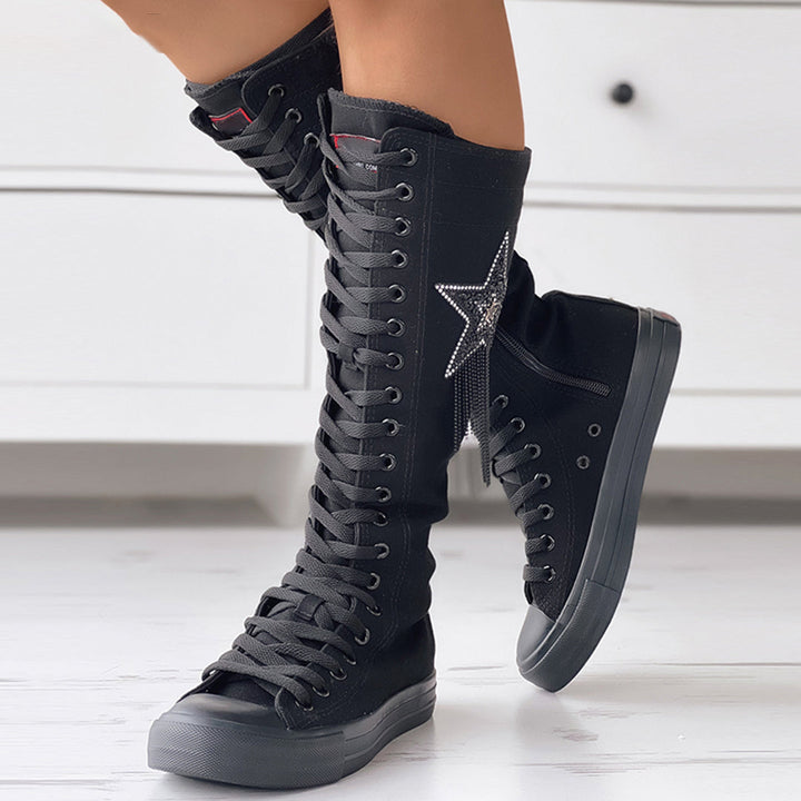 Bottes sneakers noires montantes pour femme, portées de profil avec fermeture à lacets, étoile latérale et semelle épaisse.