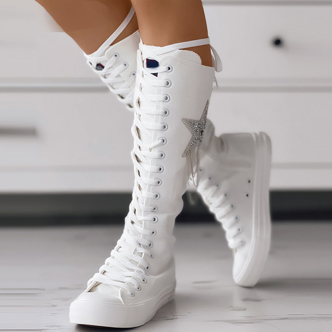 Bottes sneakers blanches montantes pour femme, portées de face avec fermeture à lacets, étoile latérale et semelle épaisse.