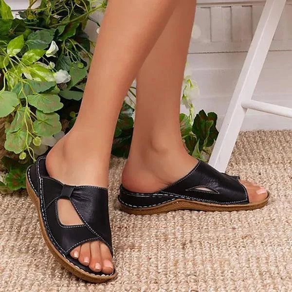 Sandales décontractées noires pour femme portées de profil en extérieur, avec brides croisées ajourées et semelle plate confortable.