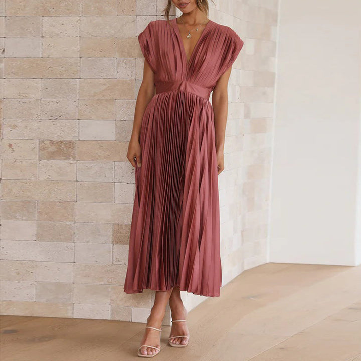 Robe longue rose rouge à col en V portée de face, avec taille marquée, jupe plissée fluide et manches courtes.