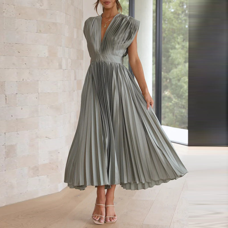 Robe longue olive à col en V portée en mouvement, avec une taille marquée et une jupe plissée fluide et évasée.