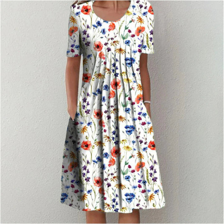 Robe d'été évasée blanche avec imprimé floral rouge, bleu et jaune, portée de face avec une coupe fluide et des manches courtes.