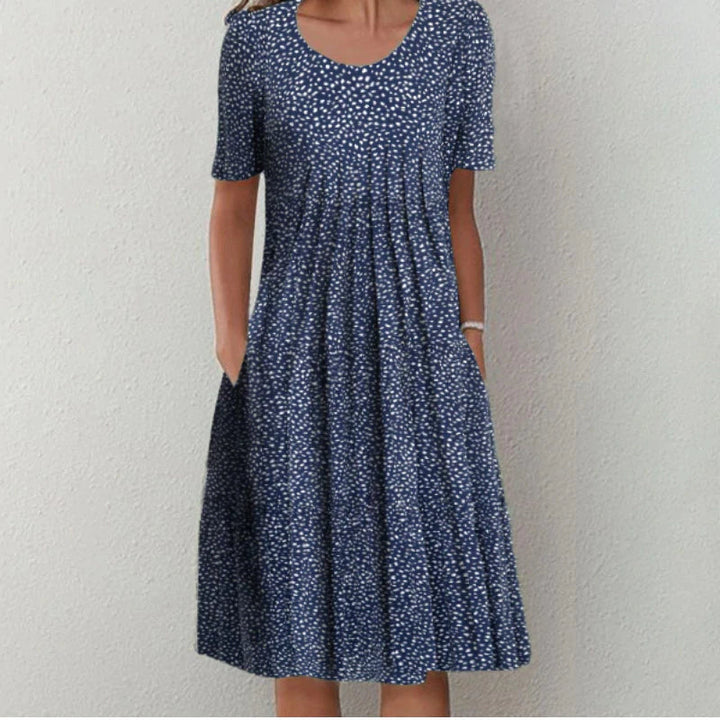 Robe d'été bleue à pois blancs, portée de face avec une coupe évasée et une longueur au genou.