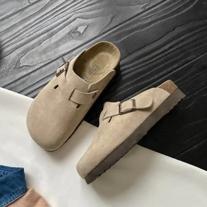 Sabots beiges avec boucle réglable présentés en paire sur un sol en bois, mettant en valeur leur design confortable.