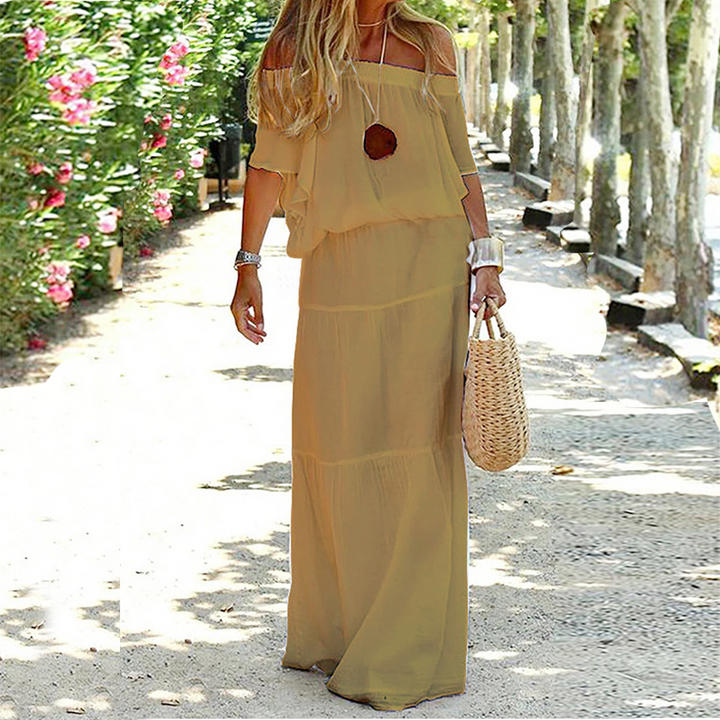 Robe longue khaki pour femme à épaules dénudées, portée de face en extérieur avec coupe fluide et longueur jusqu’aux chevilles.