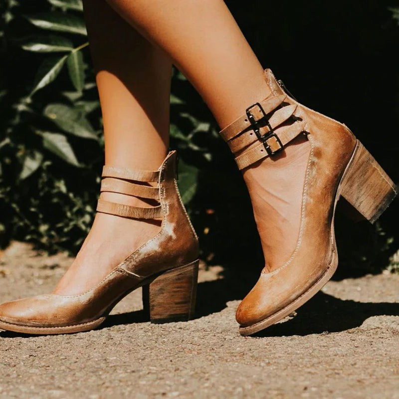 Gros plan sur des bottines marron portées en extérieur, avec brides et boucles autour de la cheville et talon épais
