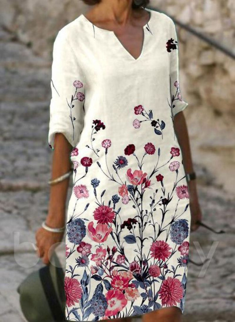 Robe élégante pour femme avec fond blanc, imprimé floral coloré, manches trois-quarts et coupe fluide photographiée en extérieur