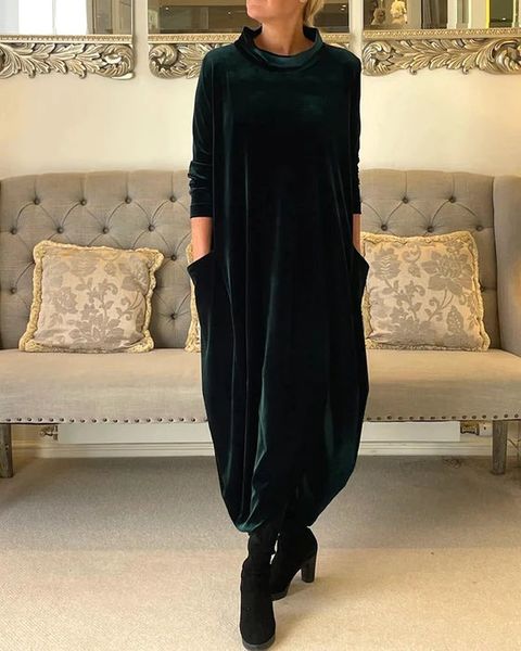 Robe longue en velours vert foncé, coupe ample manches longues, vue de face en intérieur salon, tenue élégante femme