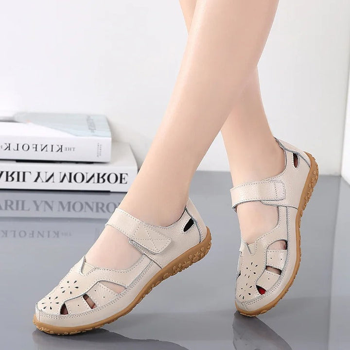 Sandales beiges à bout fermé pour femme portées de trois-quarts, avec découpes ajourées, bride réglable et semelle compensée.