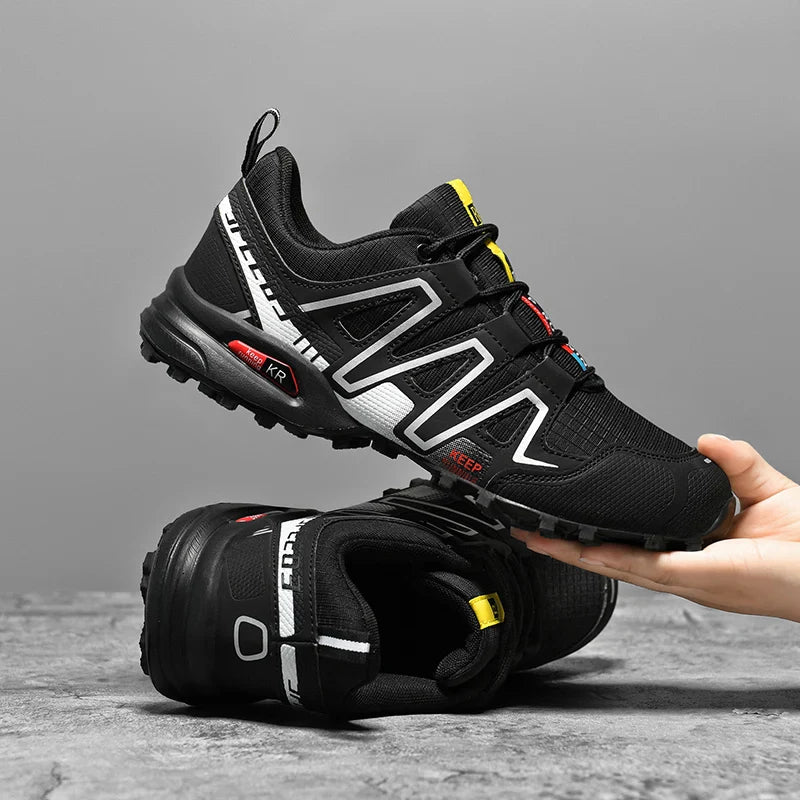 Chaussures de randonnée noires avec touches grises, photo produit en vue trois-quarts près d’un appareil photo, style trail outdoor